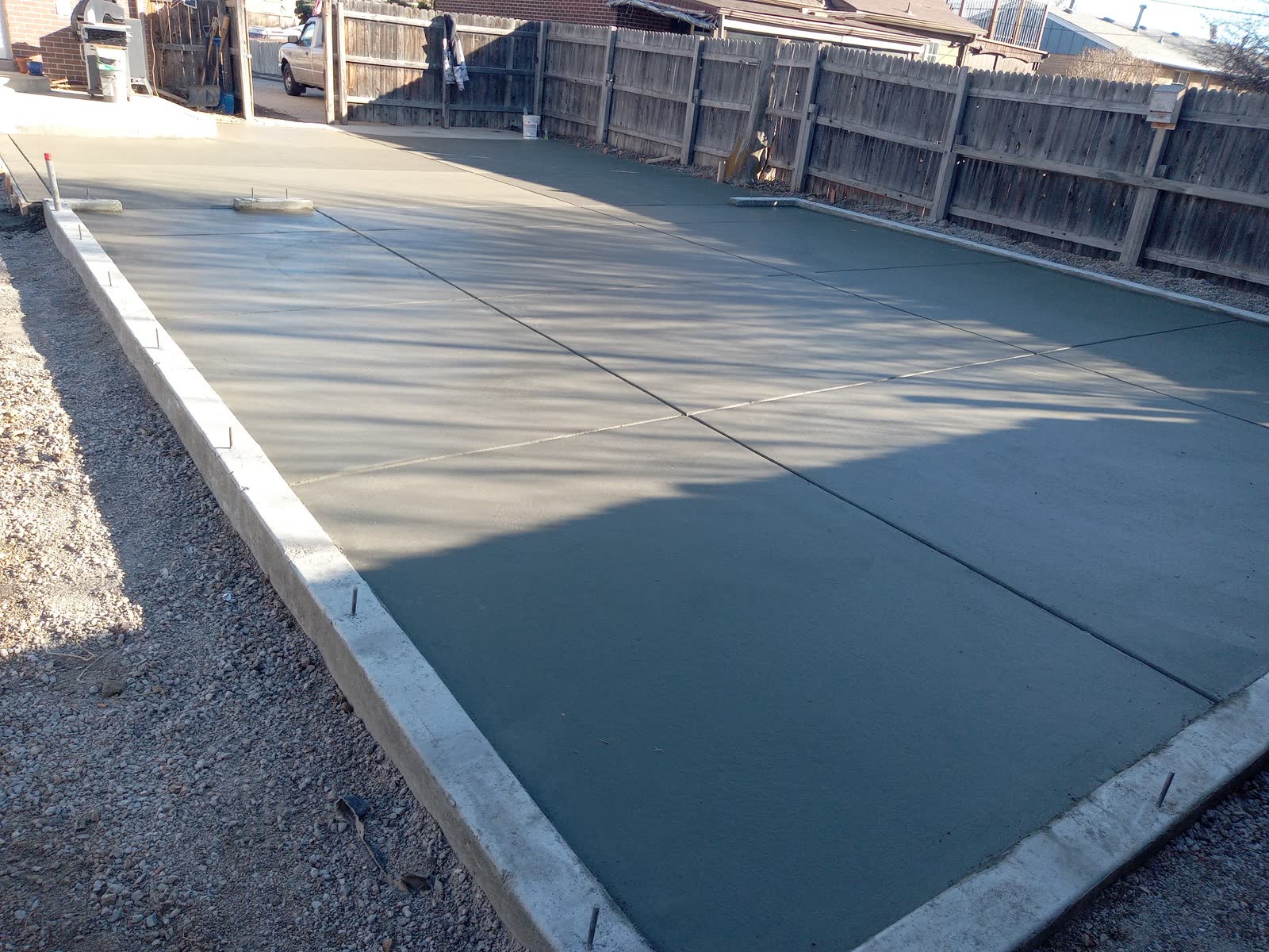 A freshly floated concrete slab curing in the afternoon sun beside a wood fence